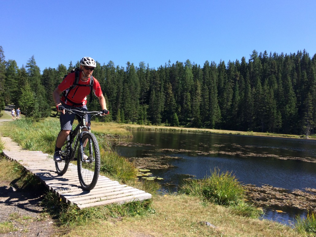 MTB-Camp Nauders Ein Biker passiert einen Holzsteg an einem See
